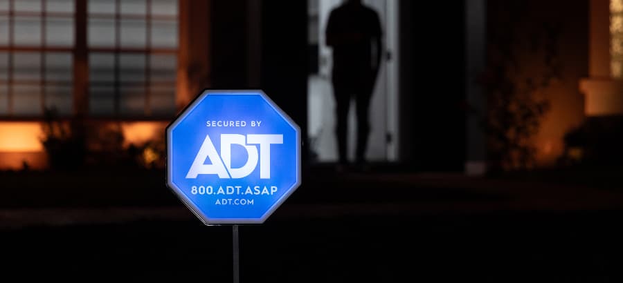 Illuminated ADT home security sign in yard of a home after dark.